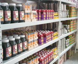 The image shows a set of organized shelves stocked with various food items, likely in a food bank or pantry. 