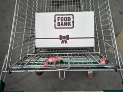 The image depicts a metal shopping trolley with a single cardboard box labeled "Foodbank" inside it.