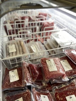 The image shows a selection of packaged meat products displayed in a refrigerator. The packages include different cuts of meat, such as ground meat and other varieties, all neatly vacuum-sealed in clear plastic. The labels on each package provide product details, likely including weight, type of meat, and perhaps price or source information. The arrangement of the packages in the refrigerator is organized, facilitating easy viewing and selection for customers. 