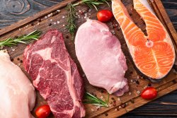 The image displays a wooden cutting board with raw chicken, beef, pork, and salmon, garnished with rosemary, cherry tomatoes, salt, and peppercorns.